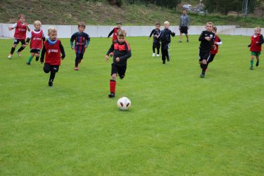 G1: Elf Mann stürmen einem Ball hinterher, der Trainer schaut zu